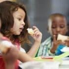 3 children of color sitting in a cafeteria eating lunch