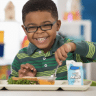 small child smiling while digging in to food on a school lunch tray