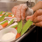 School nutrition staff placing snap peas and carrots onto lunch trays.